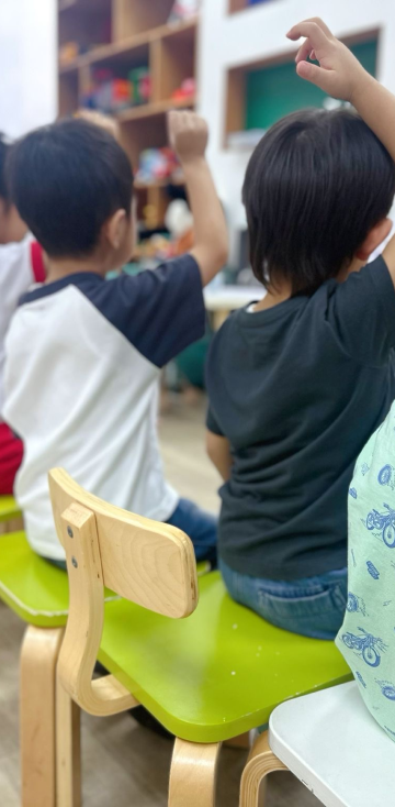 A classroom scene featuring children sitting on chairs, focused on their activities.