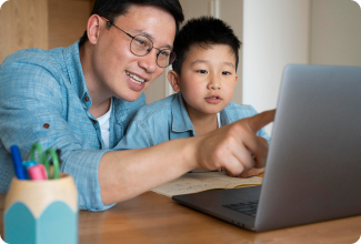 A man and a young boy gaze intently at a laptop, engaged in a shared experience of exploration