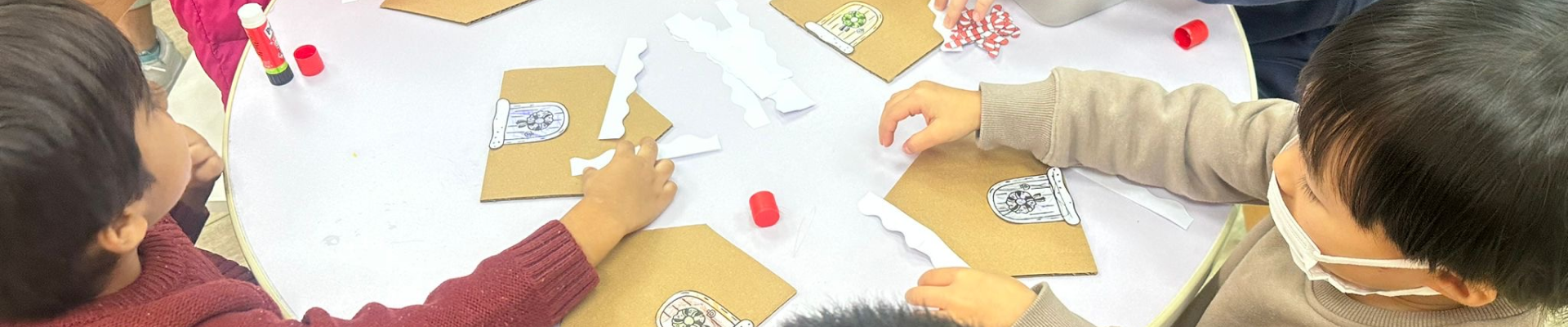 "A group of children engaged in playful creativity, cutting paper with scissors at a table filled with art supplies. "