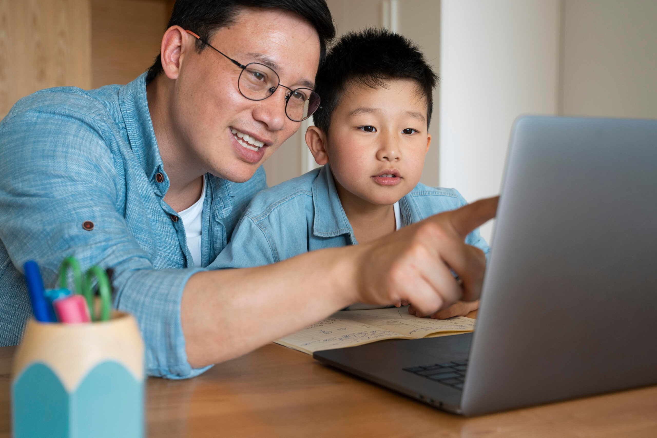 A man and a young boy gaze intently at a laptop, engaged in a shared experience of exploration
