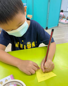 A young boy, Lukas, wearing a face mask, is engaged in writing at a table, showcasing his focus and determination.