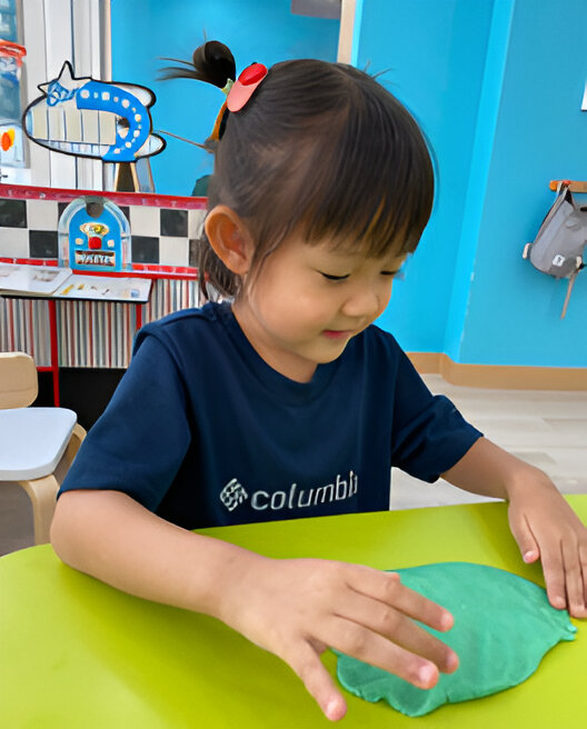 A little girl happily plays with green play dough, exploring her creativity and having fun with her hands.