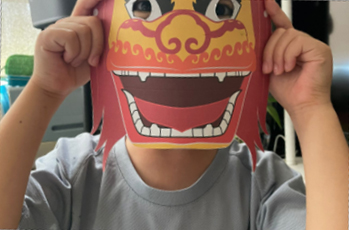 A child proudly displays a colorful paper mask featuring a vibrant Chinese dragon design.