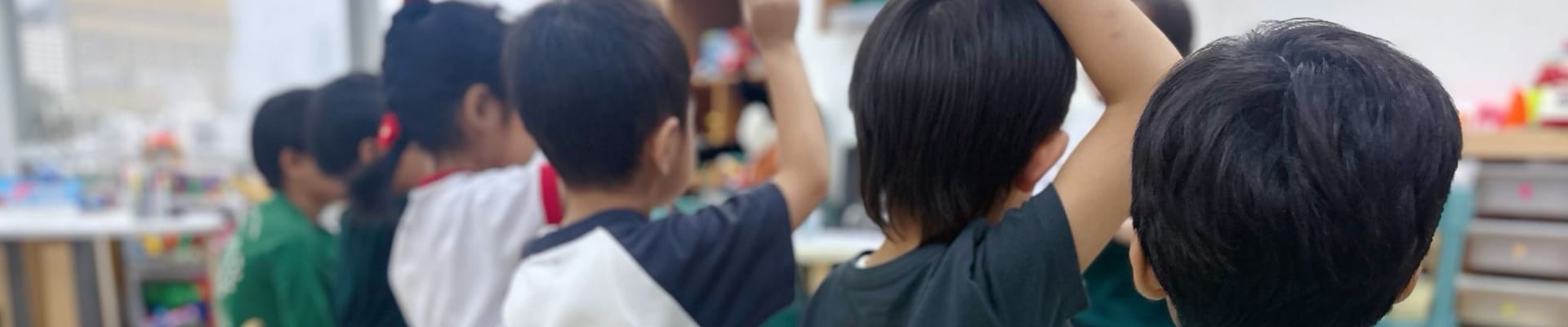A classroom scene with children at desks, raising their hands to answer questions.