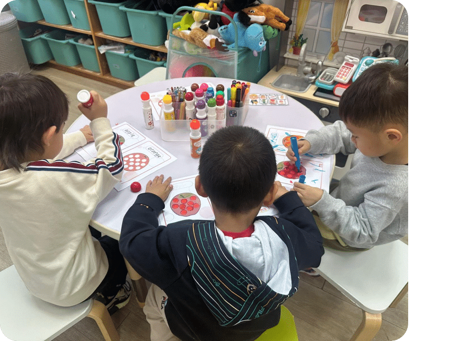 A table filled with markers and crayons as three children sit together, focused on their colorful drawings.